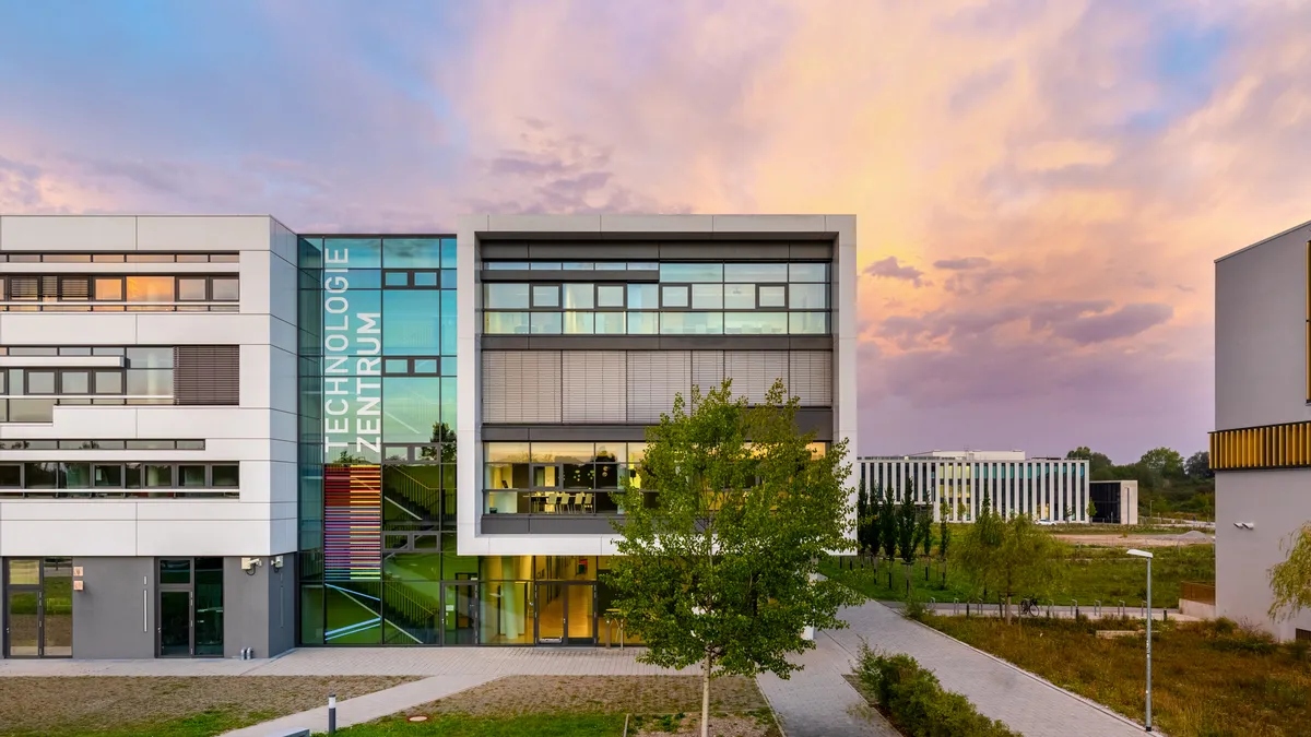 Technologiezentrum Augsburg bei Sonnenaufgang, mit dem Schriftzug „Technologiezentrum“ an der Glasfassade